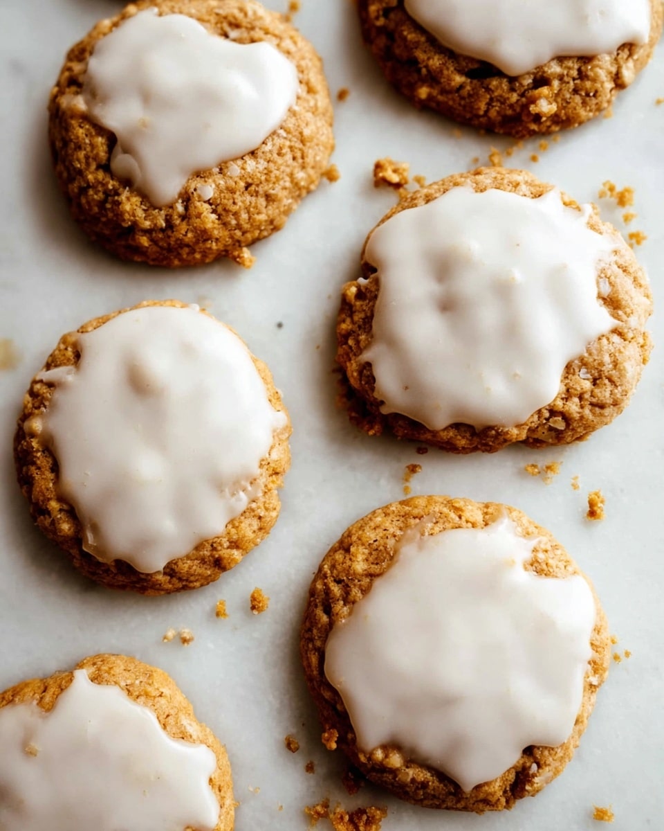 The image shows six round cookies with a rough textured, golden-brown base. Each cookie is topped with a smooth, creamy white icing that is spread unevenly, covering most of the top but leaving some of the cookie base visible around the edges. The cookies are arranged in a loose grouping on a flat white marbled surface. Crumbs from the cookies are scattered around, adding a casual, inviting feel. The scene is lit with soft natural light, highlighting the contrast between the darker cookie base and the bright icing. photo taken with an iphone --ar 4:5 --v 7
