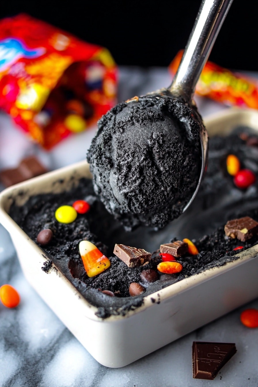 Boo Batter No-Churn Ice Cream, Halloween ice cream, no-churn Halloween dessert, easy spooky ice cream, quick no-machine ice cream - The image shows a scoop of dark black ice cream with a rough texture lifted on a metal ice cream scooper above a white dish filled with the same ice cream. The ice cream base is very dark, almost charcoal black, with visible chunks mixed inside. Around the edges of the dish, colorful candy pieces like red, yellow, orange, and white candy-coated chocolates and pieces of chocolate bars are scattered. In the background, there is a colorful, open candy bag lying on a white marbled surface. The scene has a close-up focus on the dark ice cream. photo taken with an iphone --ar 2:3 --v 7