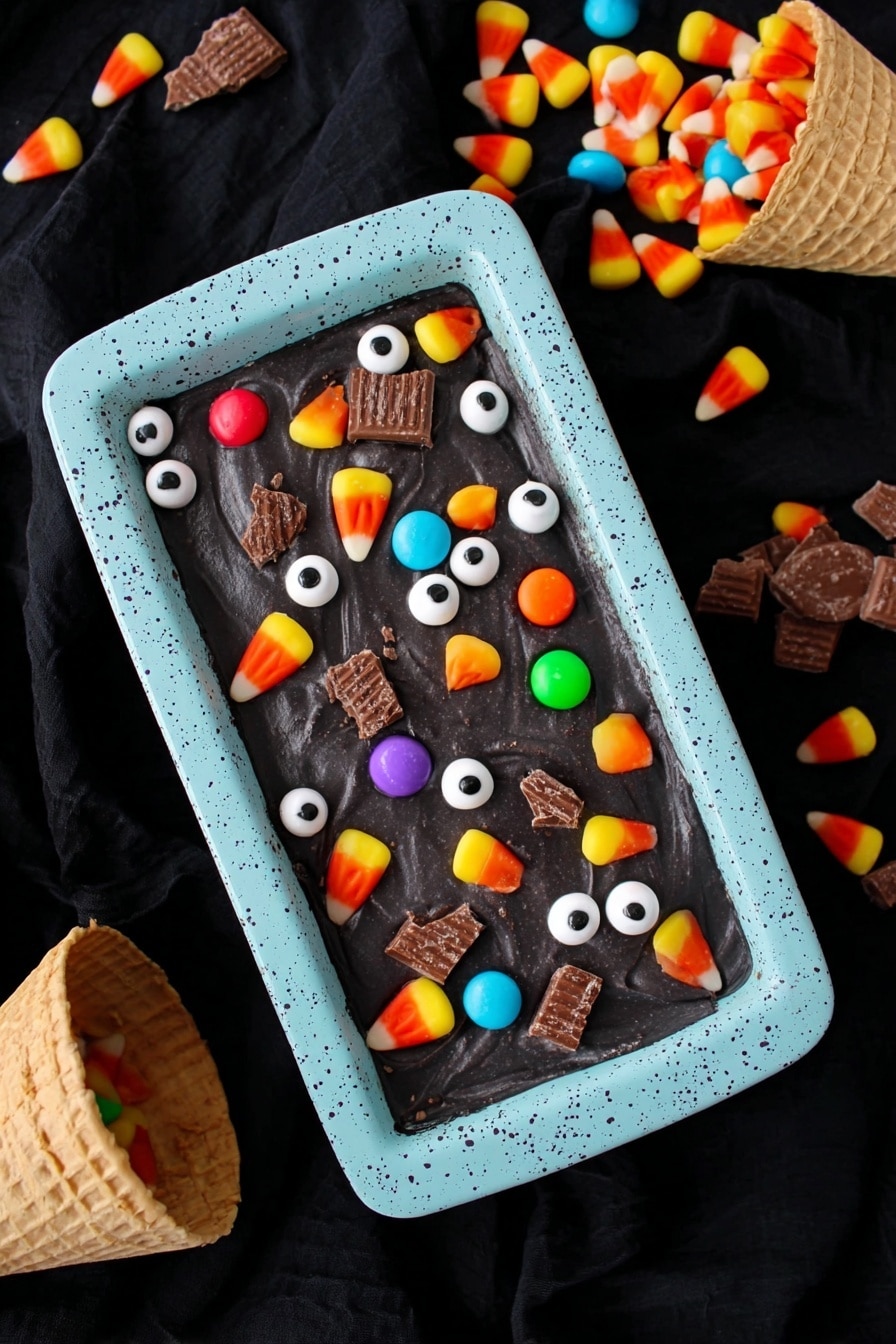 Boo Batter No-Churn Ice Cream, Halloween ice cream, no-churn Halloween dessert, easy spooky ice cream, quick no-machine ice cream - A rectangular dish with a light blue speckled container holds a smooth, dark black surface of dessert. On top, there are scattered small white candy eyeballs with black centers, colorful round candy pieces in orange, yellow, green, red, and purple, pieces of candy corn with yellow, orange, and white layers, and broken sections of chocolate wafer candy bars. The scene is against a black fabric background with two waffle cones spilling colorful candy wrappers and candy into the frame. photo taken with an iphone --ar 2:3 --v 7