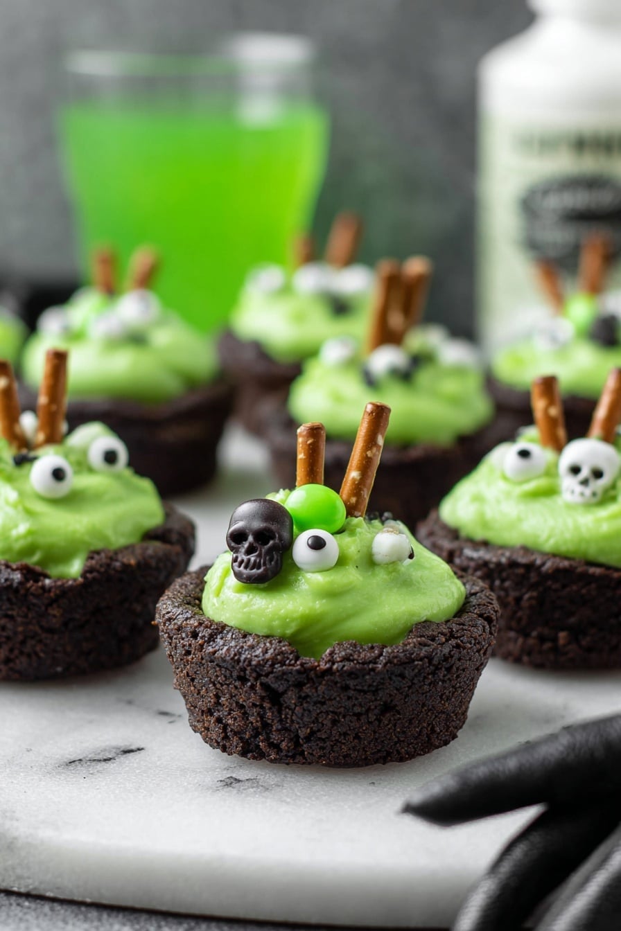 Cauldron Cookie Cups, Halloween cookie recipes, festive baking ideas, chocolate cookie cups, spooky treat ideas - The image shows small dark brown cookie cups filled with bright green creamy frosting. Each frosting has small white and green candy decorations shaped like skulls and eyeballs, giving a spooky look. A small pretzel stick is inserted into the frosting on each cup, standing upright. The cookie cups are placed on a white marbled surface, and in the background is a blurry green drink and a white bottle with black text. A woman's hand in a black glove is reaching towards the cookie cups from the right side. photo taken with an iphone --ar 2:3 --v 7