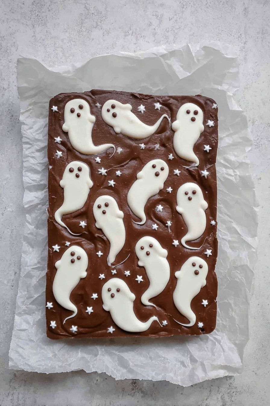 Halloween 3-Ingredient Ghost Bark, easy Halloween treats, spooky chocolate desserts, ghost-shaped candies, quick Halloween party snacks - A rectangular chocolate fudge layer placed on crinkled white parchment paper on a white marbled surface, decorated with multiple small white ghost shapes spread across the top. The ghosts are made from a white creamy layer, each with rounded heads and flowing tails with small dark eyes and mouths, giving a spooky look. Small white star-shaped sprinkles are scattered evenly across the chocolate background, adding texture and contrast. The overall look is smooth with a few swirled edges on the ghost shapes, making a playful Halloween-themed treat. photo taken with an iphone --ar 2:3 --v 7