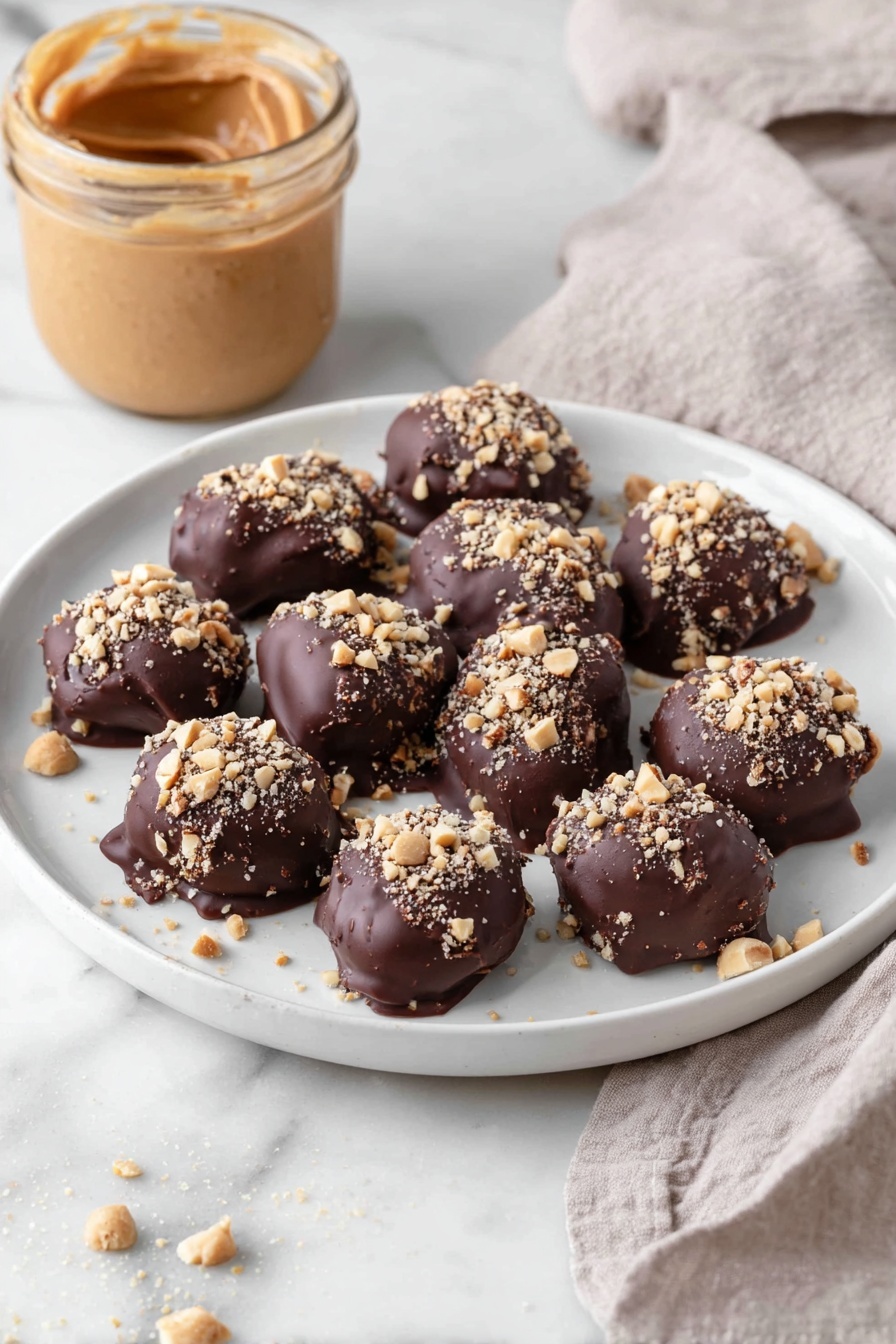 Date Snickers, no-bake date snickers, healthy date energy bites, easy chocolate date treats, homemade date snickers bars - A white plate holds eleven bite-sized treats, each covered in a thick, dark brown chocolate layer with a slightly glossy and smooth texture. On top of each piece, there is a sprinkling of small, light tan chopped nuts adding a rough, crunchy texture. The treats are arranged loosely close to each other in the center of the plate. In the background, there is an open jar filled with smooth, creamy peanut butter in a light brown shade, and a light beige cloth with a soft, woven texture lies nearby on a white marbled surface. Photo taken with an iphone --ar 2:3 --v 7