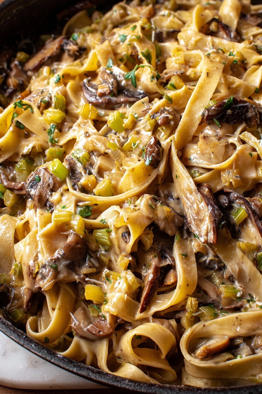 Caramelized Leek and Mushroom Fettuccine, leek and mushroom pasta, creamy vegetable pasta, gourmet fettuccine recipe, easy mushroom leek pasta - This close-up image shows a pan full of creamy pasta with broad, flat noodles tangled among large, uneven pieces of dark brown mushrooms. The sauce is light beige and coats the pasta and mushrooms, with small diced bits of green and yellow vegetables spread throughout, adding texture and color. The surface below the pan has a white marbled texture visible on the edges. photo taken with an iphone --ar 2:3 --v 7
