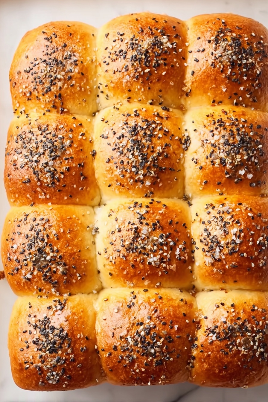 Cuban Pork Sliders, Cuban Pork Sliders Recipe, easy Cuban sliders, pulled pork sliders, party sliders - The image shows twelve soft golden-brown dinner rolls arranged in a 3 by 4 grid on a white marbled surface. Each roll has a smooth, shiny top with a slightly rounded shape, sprinkled generously with black and white sesame seeds and bits of coarse salt, giving them a textured look. The rolls fit closely together, creating visible but soft seams where they touch. The lighting highlights the warm, golden tones and the seed details clearly. Photo taken with an iphone --ar 2:3 --v 7
