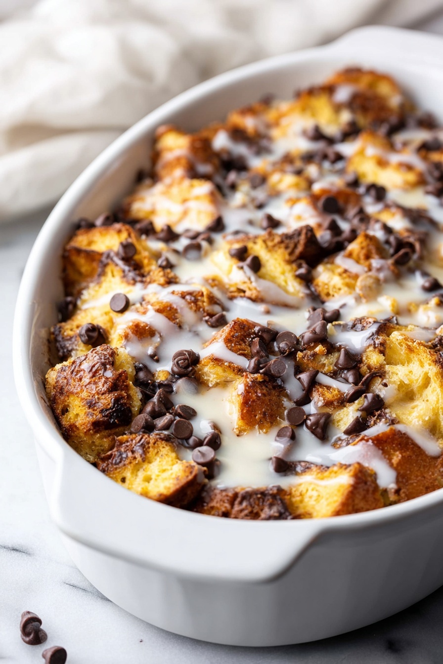 Tres Leches Bread Pudding with Chocolate Chips, Tres Leches Bread Pudding, Bread Pudding with Chocolate Chips, Easy Tres Leches Dessert, Moist Brioche Bread Pudding - A white oval dish holds a baked bread pudding with layers of golden brown, toasted bread pieces that have a slightly crunchy texture, scattered generously with dark chocolate chips that add a rich contrast. The pudding is topped with a light drizzle of white glaze, giving a shiny and smooth finish. The dish sits on a white marbled surface with part of a soft white cloth in the background. photo taken with an iphone --ar 2:3 --v 7