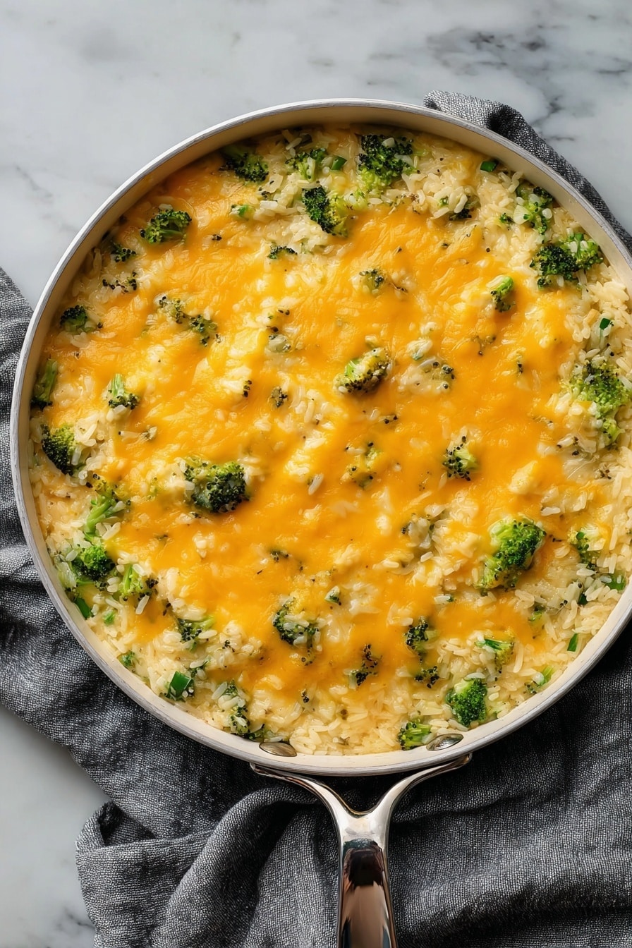 Cheesy Broccoli Rice Vegan Casserole, vegan broccoli rice bake, plant-based cheesy casserole, vegan comfort food recipes, easy vegan healthy dinner - The dish is served in a round white pan with a silver handle, placed on a gray cloth over a white marbled surface. It has two main layers: the bottom layer is a mix of cooked white rice with small pieces of broccoli, giving a textured base of green and white. The top layer is a smooth, even spread of melted orange cheese covering the rice and broccoli, with small bits of broccoli peeking through. The cheese looks soft and slightly shiny, adding a creamy contrast to the grainy rice below. photo taken with an iphone --ar 2:3 --v 7
