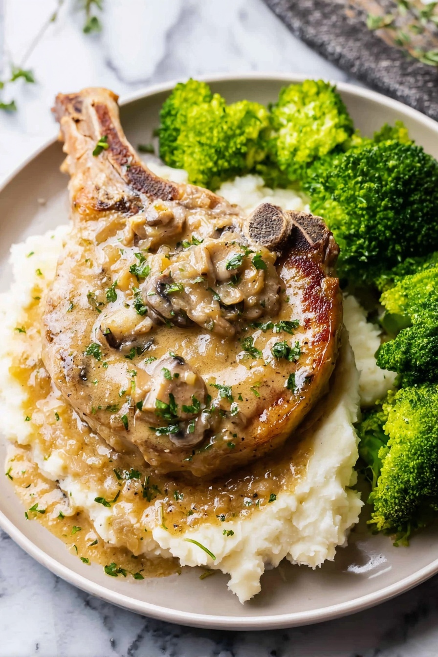 Easy Smothered Pork Chops, smothered pork chops with gravy, savory pork chop dinner, comforting pork chop recipes, easy pork chop recipe - A large cooked pork chop sits in the center of a white plate on a bed of creamy mashed potatoes as the bottom layer; the pork chop has a light brown color with a creamy mushroom sauce on top, dotted with pieces of mushrooms and sprinkled with small green herbs; to the right side of the plate, there are bright green steamed broccoli florets with a slightly wet texture; the white mashed potatoes have a soft, slightly lumpy texture, and both the pork chop and sauce have a glossy sheen from the sauce; the plate sits on a white marbled surface; photo taken with an iphone --ar 2:3 --v 7