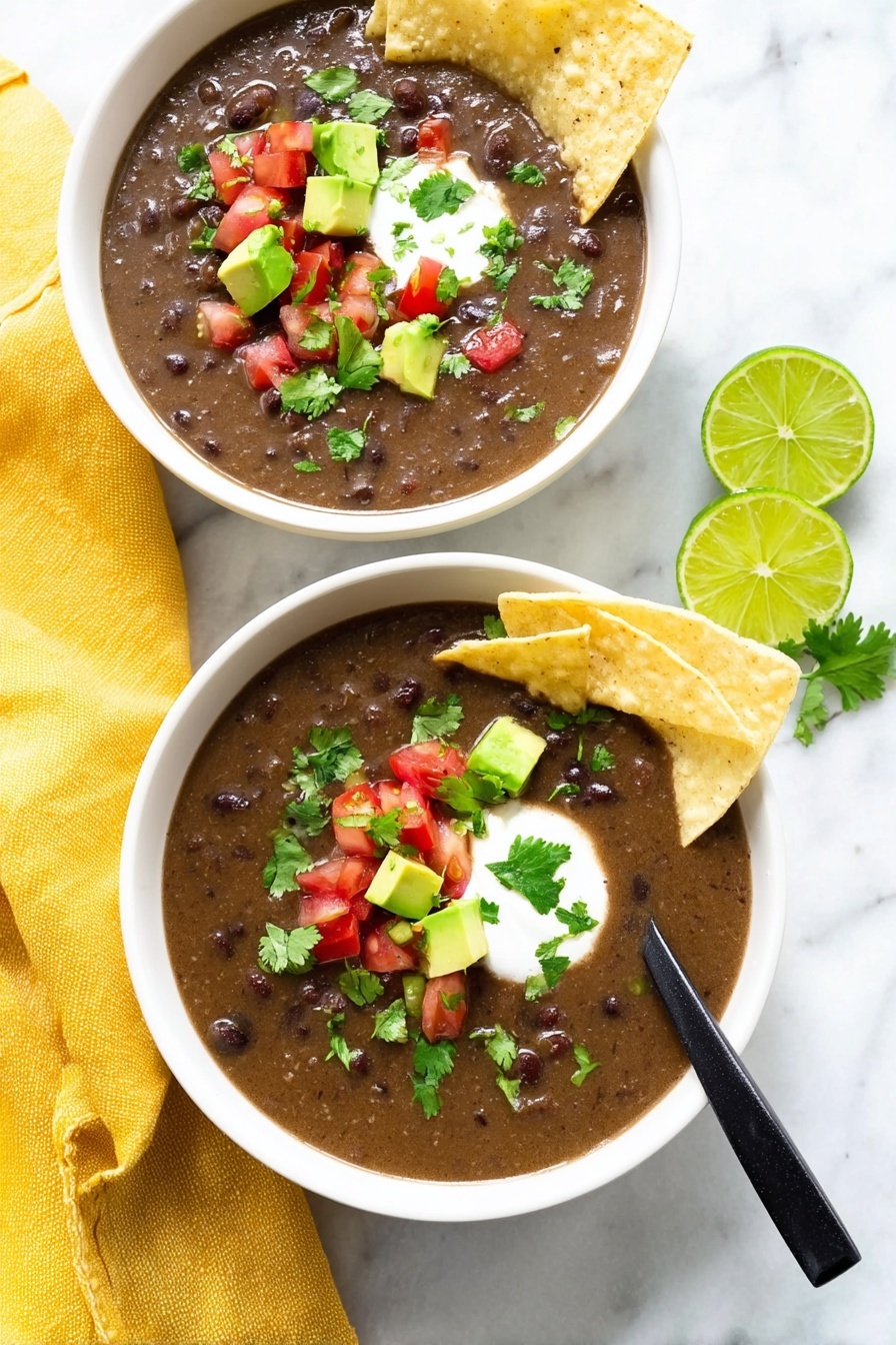 Vegan Black Bean Soup, vegan black bean soup recipe, hearty vegan soup, easy black bean soup, plant-based black bean stew - The image shows two white bowls filled with dark brown bean soup that has a thick texture. Each bowl has two light beige tortilla chips placed on the side, slightly dipped into the soup. On top of the soup, there are small cubes of bright green avocado, small pieces of red tomato, chopped green cilantro, and a dollop of white cream in the center. One bowl has a black spoon resting inside. The bowls sit on a white marbled surface with a yellow cloth napkin next to one bowl and two lime wedges nearby. The scene is bright and clean. Photo taken with an iphone --ar 2:3 --v 7
