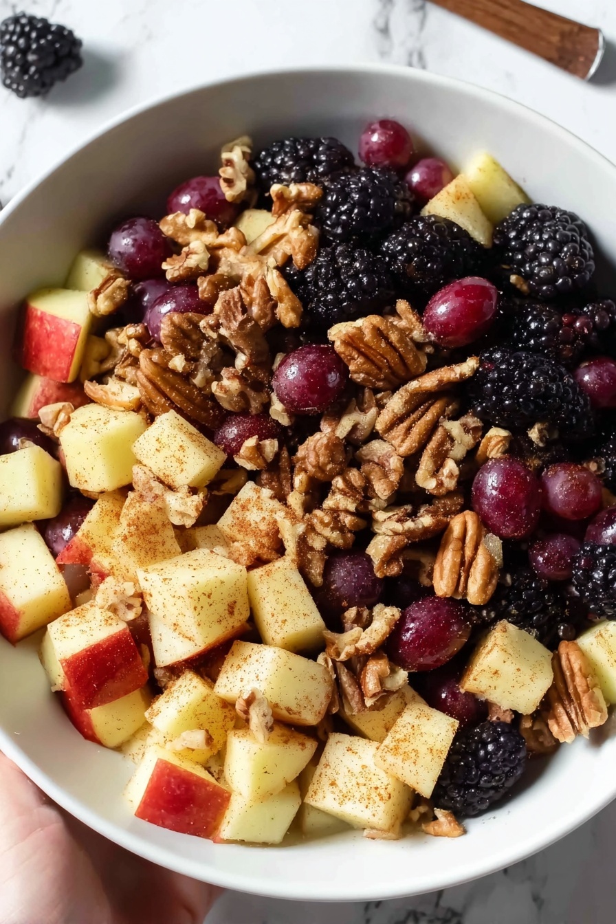 Fall Fruit Salad, fall fruit salad ideas, seasonal fruit salad, healthy fall dessert, easy fruit salad recipe - A white bowl is filled with a fruit salad that has three main layers: the bottom layer is made of blackberries, which are bumpy and dark purple-black; the middle layer has round red grapes with smooth, shiny skin; and the top layer contains apple chunks that are pale yellow with a dusting of brown cinnamon powder. Scattered throughout the salad are light brown pecans adding a rough texture. The bowl sits on a white marbled surface, and two cinnamon sticks lie nearby. photo taken with an iphone --ar 2:3 --v 7