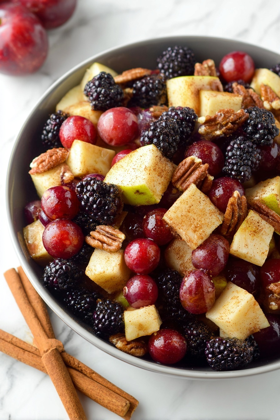 Fall Fruit Salad, fall fruit salad ideas, seasonal fruit salad, healthy fall dessert, easy fruit salad recipe - A white bowl filled with a colorful fruit and nut salad, showing three layers of ingredients. The bottom layer is pieces of pale yellow apple with red skin, cut into small cubes. The middle layer features deep red grapes and dark purple-black blackberries scattered evenly across. The top layer includes crunchy brown walnuts and pecans mixed throughout. The fruit pieces have a light dusting of cinnamon or spice, giving a slight matte texture. The bowl is placed on a white marbled surface, and a woman's hand is visible holding the bowl's edge. photo taken with an iphone --ar 2:3 --v 7