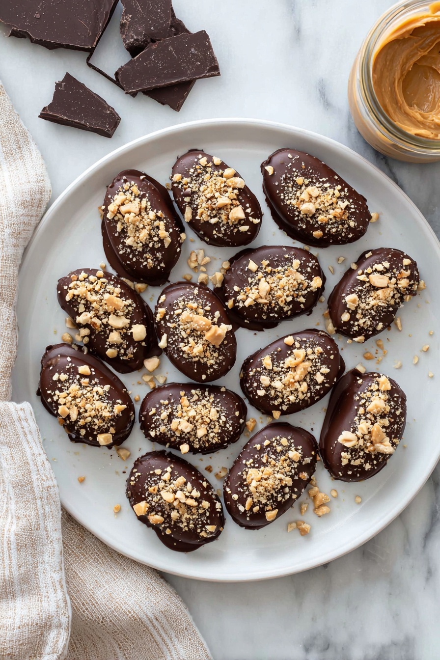 Date Snickers, no-bake date snickers, healthy date energy bites, easy chocolate date treats, homemade date snickers bars - A white plate holds a dozen small oval treats, each fully covered in smooth dark chocolate with a shiny finish. On top of every treat, there is a sprinkling of light brown crushed nuts, adding a rough texture. The plate rests on a white marbled surface, with pieces of dark chocolate on the left and a jar filled with creamy light brown peanut butter on the right side. A beige and white striped cloth is placed next to the plate on the left. photo taken with an iphone --ar 2:3 --v 7