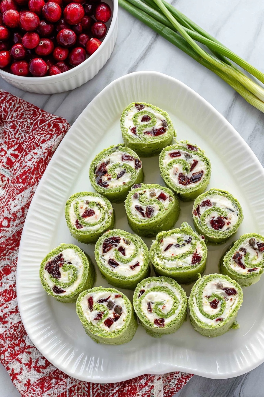 Cranberry Feta Pinwheels with Cream Cheese, holiday appetizer recipes, easy party appetizers, no-bake appetizer ideas, festive cheese and fruit snacks - On a white oval plate with a ridged edge, there are fifteen green pinwheel rolls arranged in a triangular shape, with one at the top, three in the second row, five in the third row, and six in the bottom row. Each roll shows a swirl of bright green outer layer with a creamy white filling inside that contains small pieces of dark red and green ingredients mixed throughout. The plate is placed on a white marbled surface, and to the top left, a white bowl filled with red berries is partially visible, sitting on a red and white patterned cloth. A few green onion stems lie on the top right corner of the surface. Photo taken with an iphone --ar 2:3 --v 7