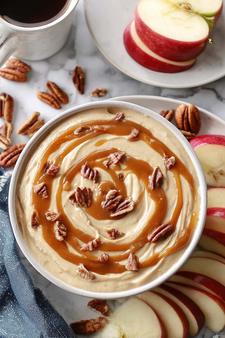 Caramel Cheesecake Dip, easy caramel cheesecake dip, no-bake caramel cheesecake, quick dessert dip, creamy caramel fruit dip - A white bowl holds a creamy beige dip that fills it nearly to the top, with smooth swirls of caramel sauce drizzled in a loose spiral on the surface. Small pieces of brown pecans are scattered evenly over the caramel, adding texture and contrast. Around the bowl, slices of red apple with white insides sit beside whole pecans. In the background, a white plate holds more apple slices, and a white marbled surface surrounds everything. A woman's hand holds a white cup filled with a dark drink near the top left corner. photo taken with an iphone --ar 2:3 --v 7