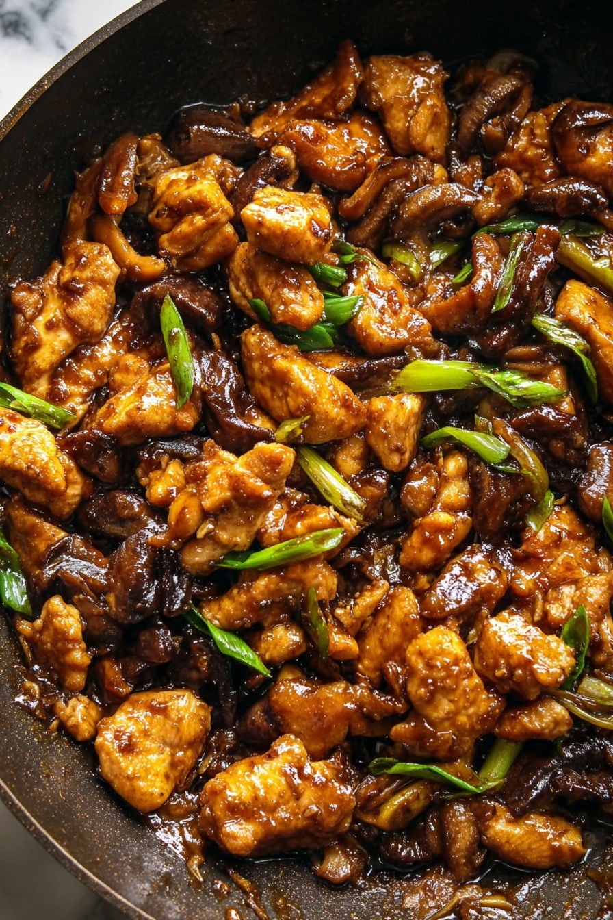 Black Pepper Mushroom Chicken Stir Fry, easy mushroom chicken stir fry, quick weeknight chicken stir fry, flavorful mushroom chicken dish, Asian-style chicken mushroom stir fry - The image shows a close-up of a dark pan filled with a rich brown stir-fry dish. The stir-fry has several layers of golden brown cooked chicken pieces that look crispy on the edges, mixed with dark brown cooked mushroom slices. Scattered throughout the dish are small pieces of bright green sliced spring onions, adding a fresh contrast. The sauce covering the ingredients is glossy and thick, giving the dish a shiny look. The background is a white marbled texture. photo taken with an iphone --ar 2:3 --v 7