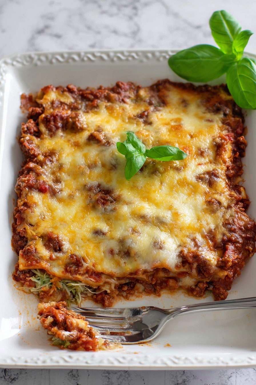 Cheesy Zucchini Pizza Casserole, zucchini casserole with cheese, homemade pizza casserole, cheesy vegetable bake, easy zucchini recipe - The image shows a white rectangular baking dish filled with a baked casserole that has three visible layers. The bottom layer is a chunky, dark brown meat sauce mixed with red tomato sauce creating a textured base. The middle layer is mostly hidden but looks to be another portion of meat sauce. The top layer is melted cheese with a mix of pale white and golden yellow colors, slightly browned in spots. Small green basil leaves are scattered on top, adding color contrast. In the bottom left corner, a metal spatula with a white handle is partially inserted under the casserole, revealing the inside layers and the rich texture of the dish. The dish is set on a white marbled surface. Photo taken with an iphone --ar 2:3 --v 7
