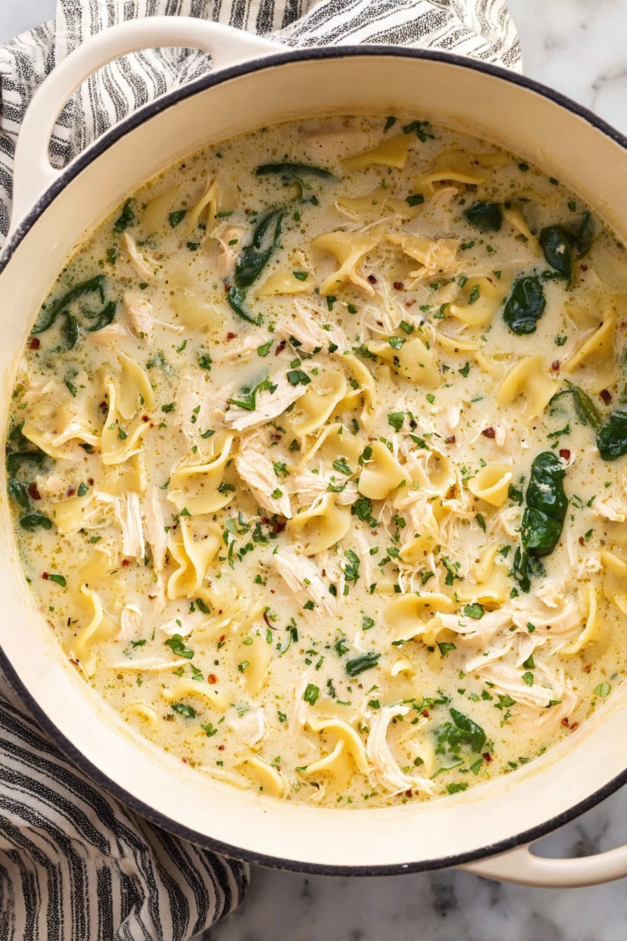 White Lasagna Soup, creamy lasagna soup, easy lasagna soup, chicken lasagna soup, comforting soup recipes - A white pot filled with creamy soup that has three main layers: shredded white chicken pieces spread evenly, dark green spinach leaves scattered throughout, and curly, pale yellow pasta floating in a thick, light cream broth with small herbs sprinkled all over. The pot is placed on a white marbled surface with a striped cloth under one side. Photo taken with an iphone --ar 2:3 --v 7