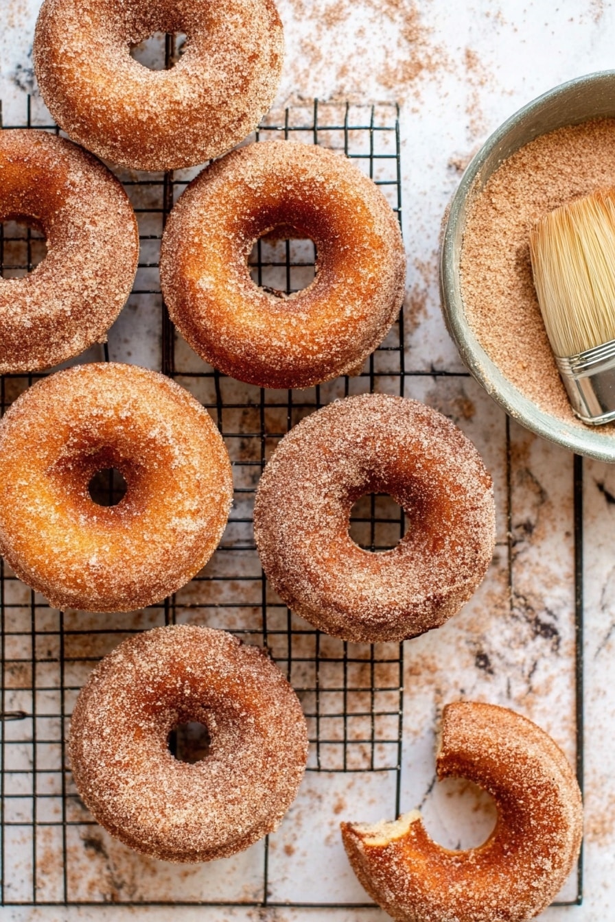 Cinnamon Sugar Doughnuts, homemade doughnuts, fluffy doughnut recipes, cinnamon sugar coating, best doughnut recipe - Seven cinnamon sugar donuts are arranged loosely on a black wire cooling rack. Each donut has a smooth, light brown surface coated with a fine layer of cinnamon sugar that gives a slightly grainy texture. The donuts have a soft, round shape with a distinct hole in the middle, and their edges are gently rounded. The cooling rack sits on a white marbled surface, which contrasts softly with the warm colors of the donuts. photo taken with an iphone --ar 2:3 --v 7