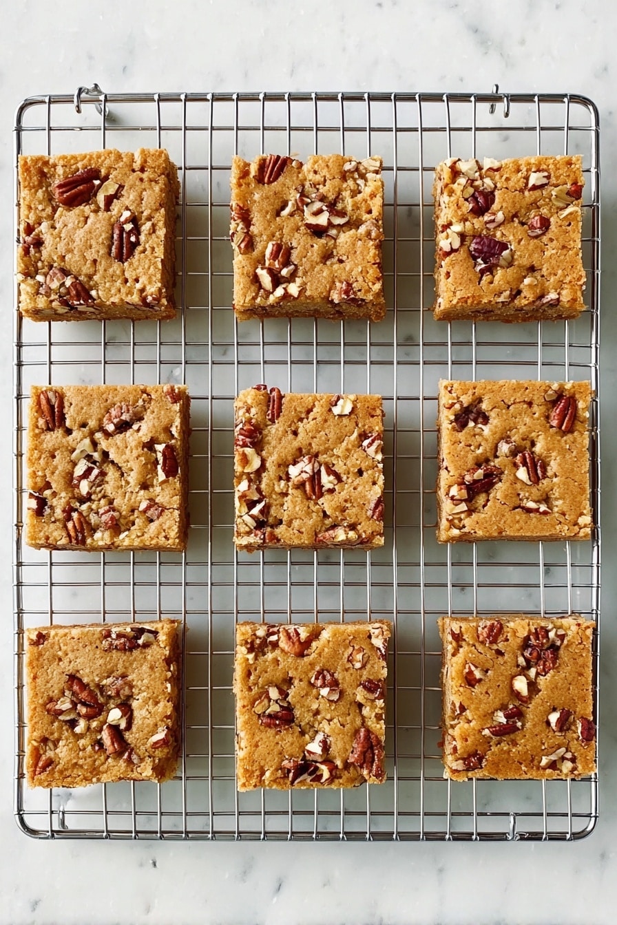 Maple Pecan Blondies, maple blondie recipe, nutty blondie bars, caramel pecan blondies, buttery dessert bars - Nine square pieces of light brown nut bars sit on a silver cooling rack. Each bar has small, uneven chunks of pecans scattered on top, creating a rough texture. The bars are evenly spaced in three rows and three columns, showing a soft, baked surface. The background is a white marbled texture. Photo taken with an iphone --ar 2:3 --v 7