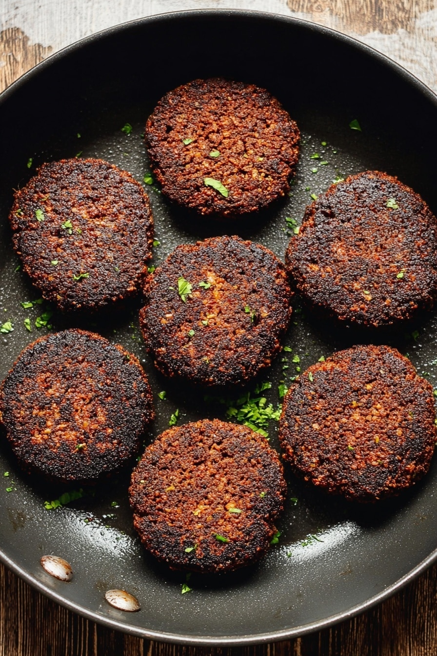 Vegan Breakfast Sausage, plant-based sausage patties, vegan breakfast ideas, homemade vegan sausage, meatless breakfast recipes - The image shows eight dark brown, crispy patties arranged evenly inside a black round pan. The patties have a coarse texture with some small bits visible, and are sprinkled lightly with small green herb pieces. The background surface seen at the top is wooden but will be imagined as a white marbled texture. The pan has a slightly shiny area where the light reflects. photo taken with an iphone --ar 2:3 --v 7