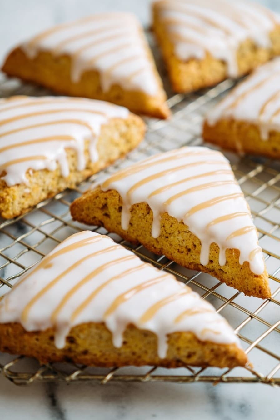 Starbucks Copycat Vegan Pumpkin Scones, vegan pumpkin scones recipe, fall vegan baked goods, vegan pumpkin spice pastries, dairy-free pumpkin scones - The image shows a close-up of several triangular scones placed on a wire cooling rack over a white marbled surface. Each scone has a golden-brown, slightly rough texture base with a smooth, thick white icing layer covering the top. Over the white icing, there are thin, even lines of light brown drizzle arranged diagonally from one corner to the other. The scones are arranged in a casual pattern, filling the frame with their detailed textures and colorful toppings. photo taken with an iphone --ar 2:3 --v 7