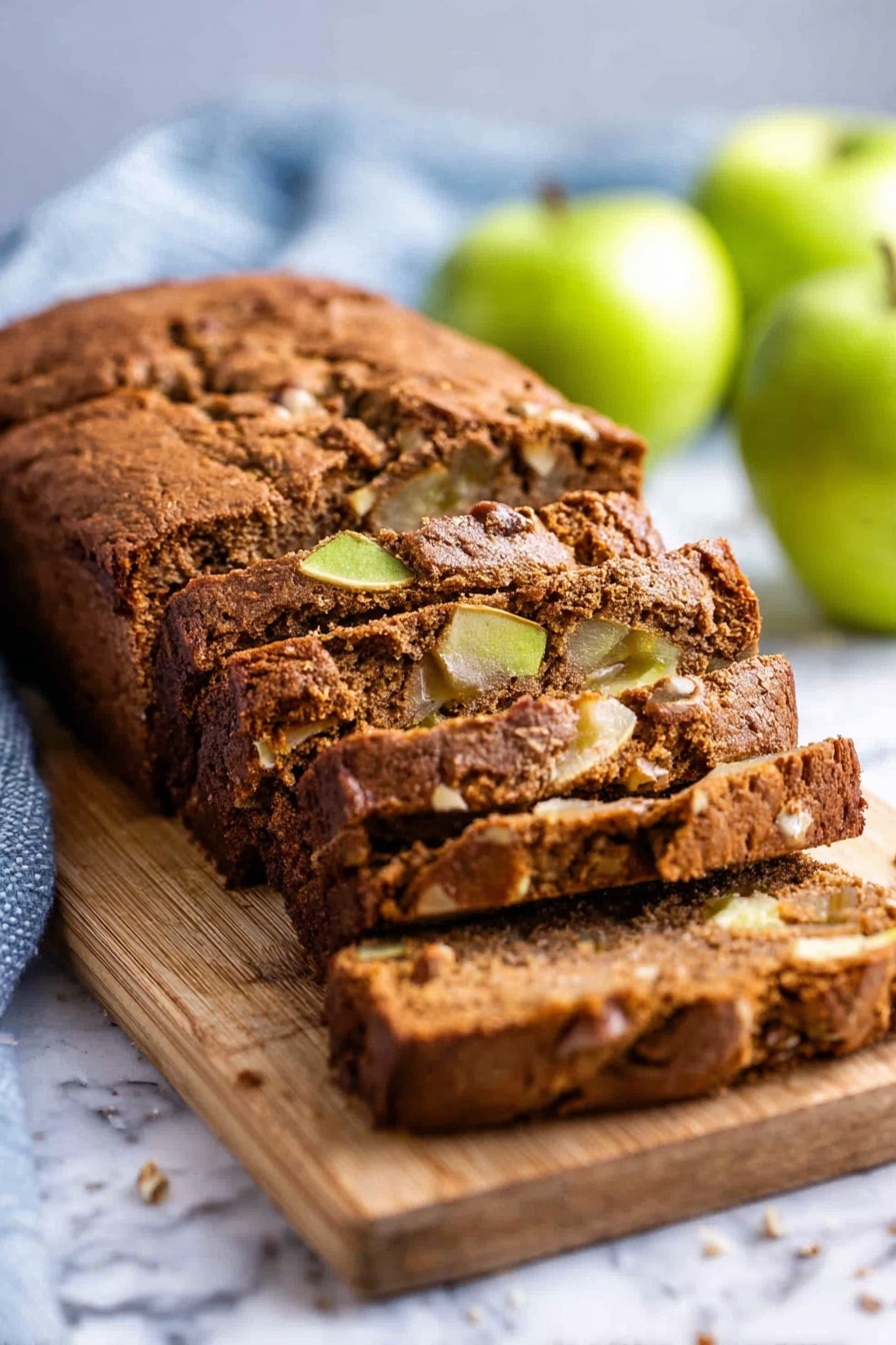 Moist Cinnamon Apple Bread, cinnamon apple bread, fall apple bread, moist apple bread, cozy cinnamon bread - A loaf of brown apple bread with a soft, cracked crust sits on a wooden board placed on a white marbled surface. The bread is sliced into thick pieces, revealing a moist inside with chunks of green apple and nuts scattered throughout. The background has a few whole green apples and a light blue kitchen towel, slightly blurred to keep the focus on the bread. photo taken with an iphone --ar 2:3 --v 7