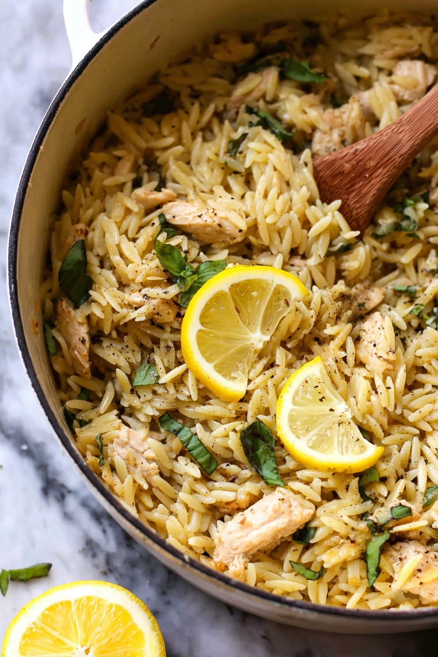 Lemon Chicken and Orzo, Lemon Chicken and Orzo dinner, easy lemon chicken pasta, one-pan lemon chicken, quick lemon chicken recipes - The image shows a white pot filled with cooked orzo pasta mixed with small pieces of light brown chicken and fresh green basil leaves scattered throughout. Two bright yellow lemon slices rest on top as a garnish, and there are visible specks of black pepper sprinkled across the dish. A wooden spoon stirs the orzo on the right side, and a lemon wedge is blurred in the white marbled background. The texture of the orzo looks soft and slightly shiny, mixing well with the tender chicken pieces. photo taken with an iphone --ar 2:3 --v 7