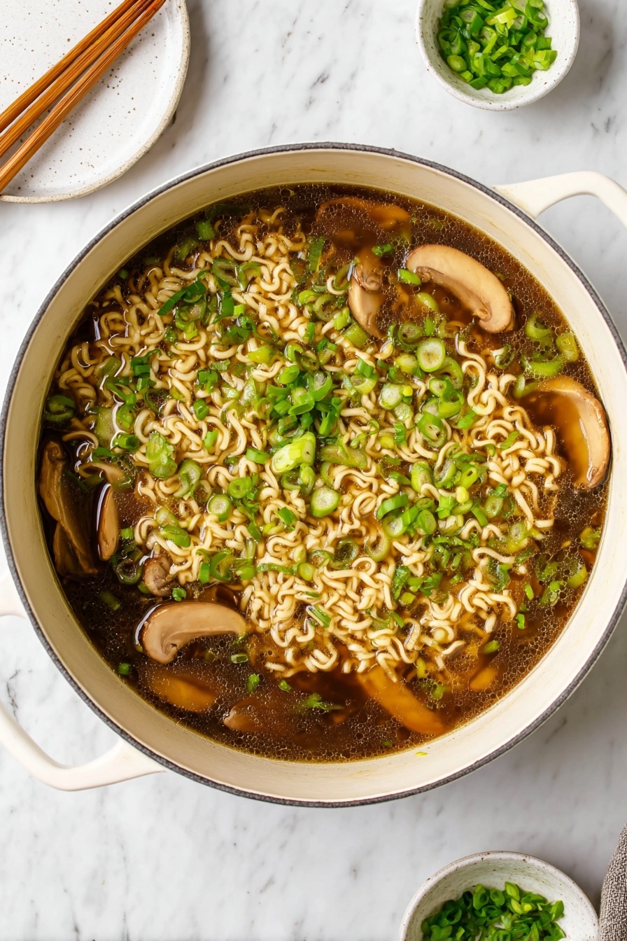 Vegan Ramen, Easy Vegan Ramen, Plant-Based Ramen, Quick Vegan Noodles, Vegan Soup Recipes - A large white pot filled with dark brown broth containing light beige cooked curly noodles scattered throughout. Several slices of light brown mushrooms float on top, mixed with plenty of bright green chopped scallions spread evenly across the surface. The pot handles are visible on the sides, resting on a white marbled surface. In the background, a round white plate with wooden chopsticks rests towards the top left, and a small white bowl with extra chopped scallions sits on a matching saucer towards the top right. photo taken with an iphone --ar 2:3 --v 7