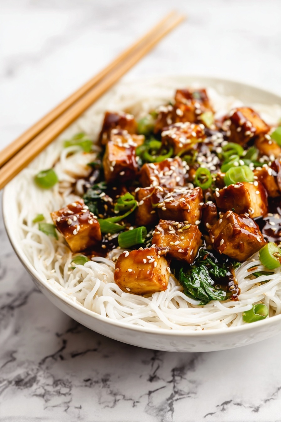 Quick One Pan Tofu Stir Fry, healthy tofu stir fry recipe, easy vegetarian dinner, quick weeknight stir fry, flavorful tofu stir fry - A white bowl is filled with thin white noodles forming the base layer. On top, there are medium-sized golden brown tofu cubes coated in a shiny dark brown sauce. Bright green chopped scallions and spinach leaves are mixed in with the tofu. White sesame seeds are sprinkled over the tofu pieces, adding texture and color contrast. Wooden chopsticks rest on the edge of the bowl over a white marbled surface in the background. Photo taken with an iphone --ar 2:3 --v 7