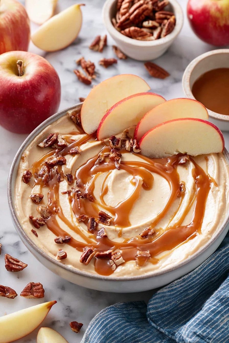 Caramel Cheesecake Dip, easy caramel cheesecake dip, no-bake caramel cheesecake, quick dessert dip, creamy caramel fruit dip - A white bowl filled with smooth, creamy light beige dip swirled on top, drizzled generously with rich caramel syrup in a circular pattern. Small pieces of chopped dark brown pecans are scattered over the dip, and slices of red apple with light yellow flesh are placed around the edge, some resting in the dip. In the background, whole and sliced apples and extra pecans are scattered on a white marbled surface, next to a small white bowl with more pecans and a small white bowl filled with caramel sauce. A blue-striped cloth is partially visible at the bottom right. Photo taken with an iphone --ar 2:3 --v 7