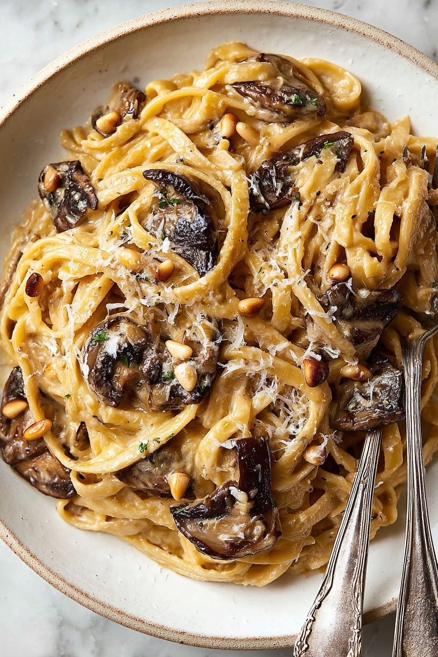 Caramelized Leek and Mushroom Fettuccine, leek and mushroom pasta, creamy vegetable pasta, gourmet fettuccine recipe, easy mushroom leek pasta - A white plate holds a dish of fettuccine pasta mixed with a creamy light brown sauce. The pasta strands are soft and twisted around each other, topped with several pieces of dark brown, slightly crispy mushrooms scattered on top and inside. Small tan pine nuts and grated pale yellow cheese are sprinkled evenly over the pasta. To the right side of the plate, two silver forks with delicate patterns rest partially on the pasta. The plate sits against a white marbled surface. Photo taken with an iphone --ar 2:3 --v 7