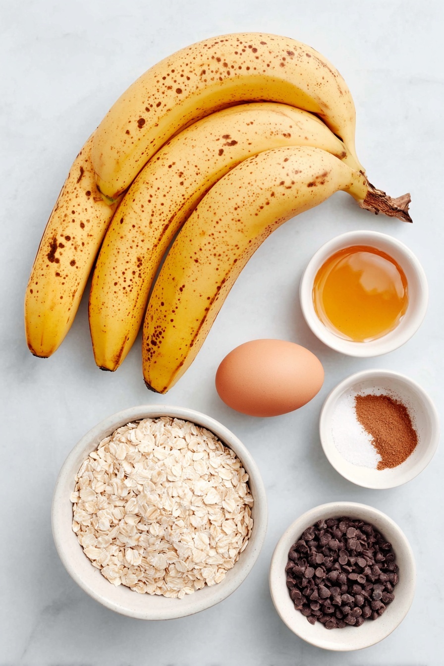 Banana Oatmeal Cookies, healthy banana cookies, easy oatmeal cookies, wholesome snack recipes, naturally sweetened cookies - Flat lay of three overripe yellow bananas with brown spots, a small white ceramic bowl of golden honey, one whole uncracked brown egg, a small white ceramic bowl filled with quick cooking oats, a small white ceramic bowl containing ground cinnamon powder, a small white ceramic bowl of fine sea salt, and a small white ceramic bowl holding dark chocolate chips, all arranged with perfect symmetry and balanced proportions placed on a clean white marble surface, soft natural light, photo taken with an iPhone, professional food photography style, fresh ingredients, white ceramic bowls, no bottles, no duplicates, no utensils, no packaging --ar 2:3 --v 7 --p awthu7i m7354615311229779997