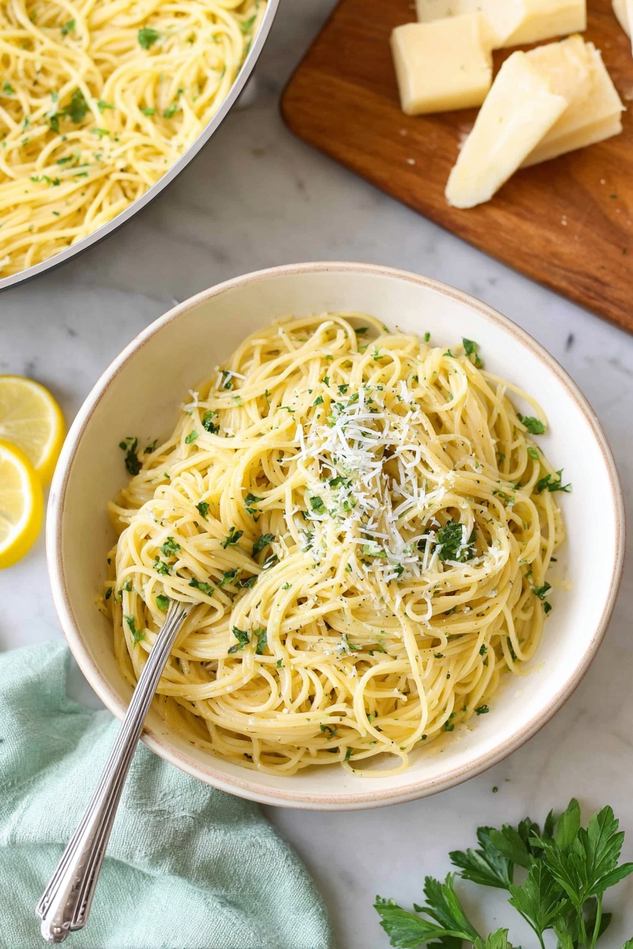 Lemon Pasta with Garlic and Parmesan, lemon pasta recipe, garlic parmesan pasta, quick lemon pasta, easy pasta dinner - A white bowl filled with light yellow spaghetti pasta mixed with small green herb bits, topped with fine white cheese shavings and fresh green parsley. On the side of the pasta are two lemon wedges. A silver fork rests inside the pasta on the left side. In the background, there is a white pan with more spaghetti and a wooden board with chunks of light yellow cheese and green parsley on a white marbled surface. A light green cloth is near the bottom left corner. Photo taken with an iphone --ar 2:3 --v 7