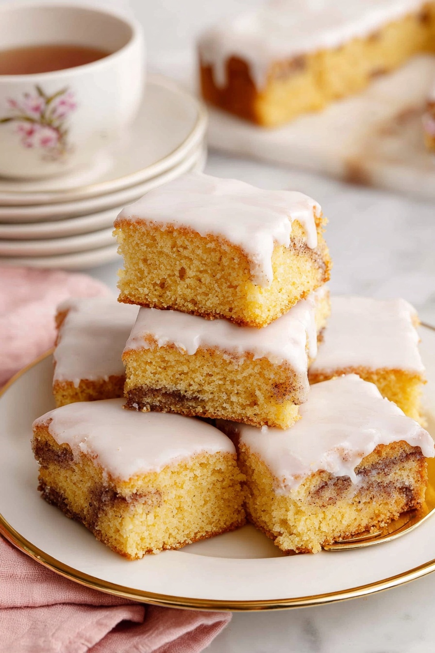 Cinnamon Roll Cake, easy cinnamon roll cake, moist cinnamon cake, cinnamon swirl cake, breakfast cake recipes - The image shows a close-up of a square piece of cinnamon roll cake with three layers: a light golden brown cake base with swirls of dark cinnamon running through the middle, topped with a thick, white creamy icing that smoothly covers the top and slightly drips down the sides. The piece sits on a small, white plate with delicate floral and butterfly decorations and a thin gold rim. In the background, there is a white plate with several more pieces of the same cake stacked slightly on top of each other. To the right, a white teacup with a gold rim and small bee design is filled with dark tea. A gold fork lies on a soft pink cloth to the side, and all items rest on a white marbled textured surface. photo taken with an iphone --ar 2:3 --v 7