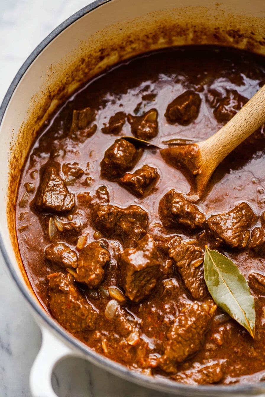 German Beef Goulash, hearty beef goulash recipe, authentic German goulash, easy beef goulash, comfort food German dish - The image shows a white pot filled with thick, brown beef stew with visible chunks of meat and a few pieces of bay leaf. The stew looks rich and glossy with a hearty texture, and there is a wooden spoon partly dipping into it on the right side. The pot sits on a white marbled surface, and the stew has dark brown and reddish hues with small bits of onions and spices mixed in. Photo taken with an iphone --ar 2:3 --v 7