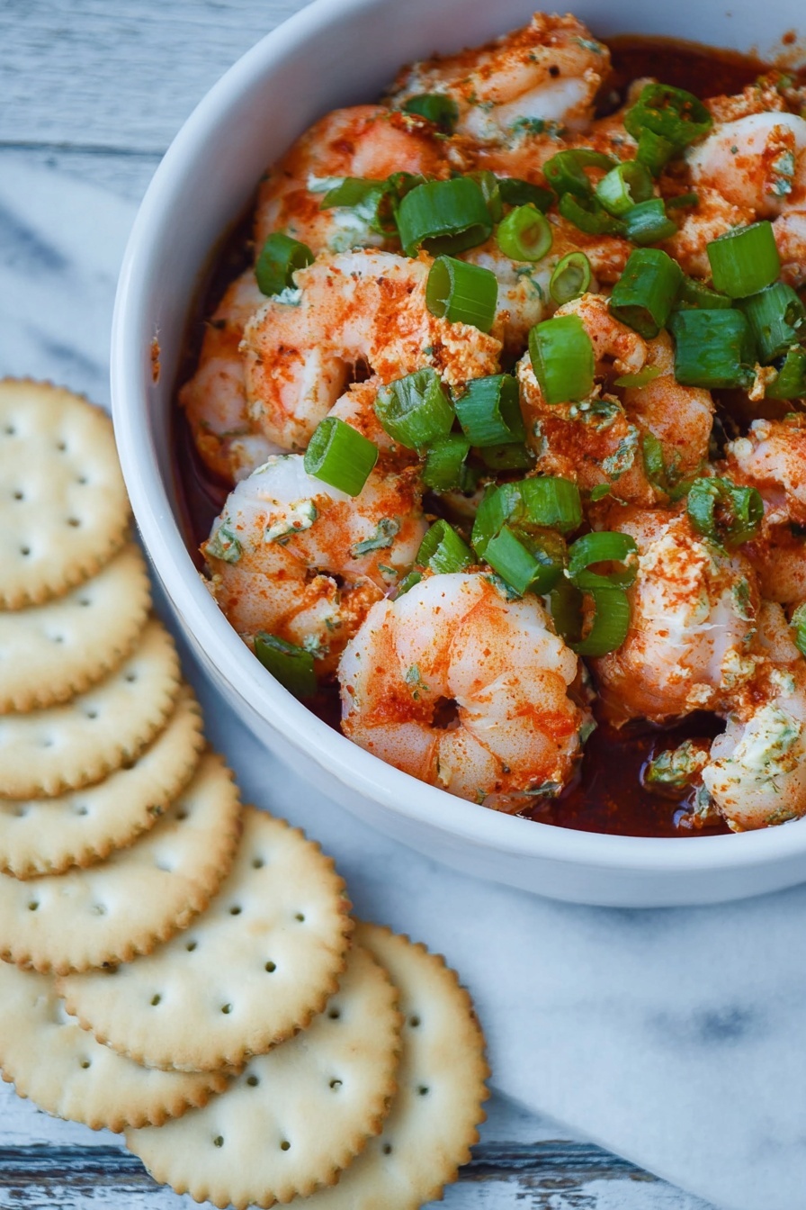 Shrimp Cocktail Dip, shrimp cocktail dip recipe, easy shrimp dip, seafood appetizer dip, party dip recipes - The dish shows one white bowl filled with three visible layers: a bottom layer of dark red sauce, a middle layer of pink and white cooked shrimp coated lightly in red spices, and a top layer of bright green chopped scallions scattered evenly over the shrimp. The textures include soft, plump shrimp with some seasoning powder visible and fresh, crisp scallions. The bowl is on a surface of white marbled texture, next to a semi-circle of pale golden round crackers arranged closely in front of the bowl. photo taken with an iphone --ar 2:3 --v 7