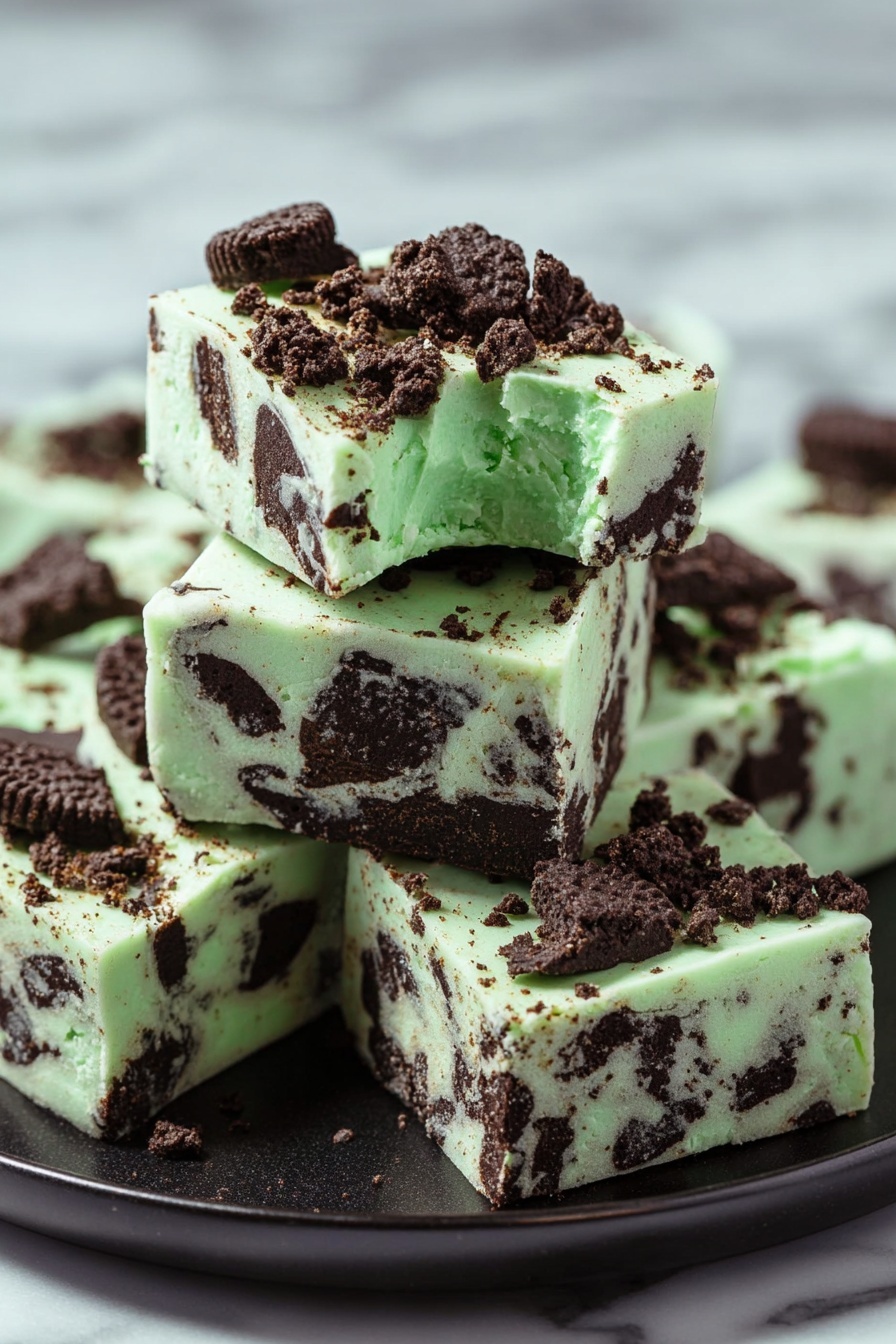 Mint Oreo White Chocolate Fudge, Mint Oreo Fudge, White Chocolate Oreo Candy, Easy Mint Fudge, No-Bake Oreo Fudge - The image shows a stack of five square pieces of mint chocolate fudge on a black plate, placed on a white marbled surface. The fudge has a pale green base with dark brown chunks of cookie mixed in all layers. On the top, bigger cookie pieces and crumbs are scattered, adding texture and color contrast. Each piece is thick and smooth with distinct edges, and the top piece has a small bite taken from its corner, showing a creamy interior with visible cookie pieces inside. Photo taken with an iphone --ar 2:3 --v 7