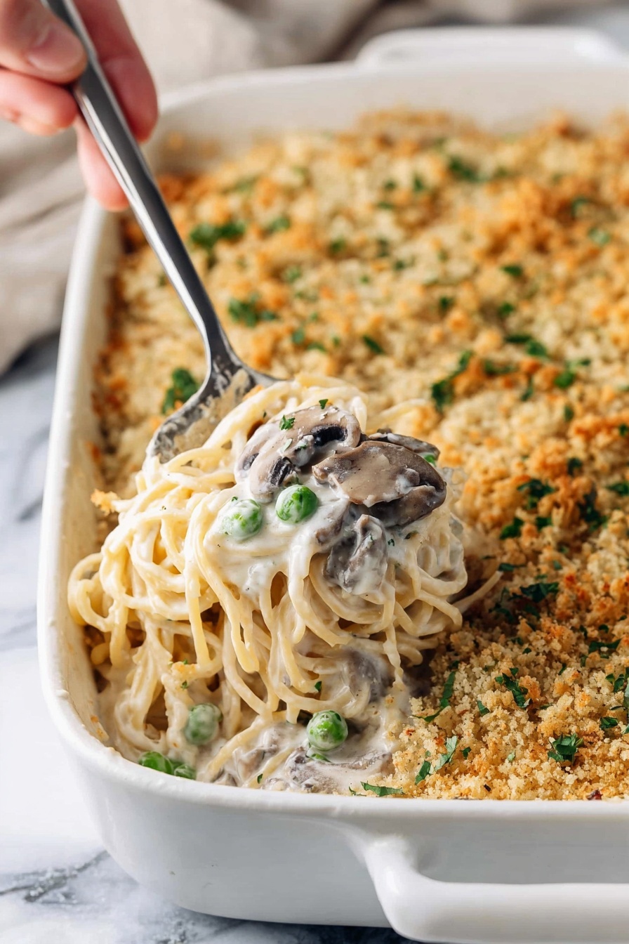 Creamy Turkey Tetrazzini Bake, Turkey Tetrazzini casserole, easy Turkey Tetrazzini, comforting pasta bake, cheesy turkey casserole - A white baking dish filled with creamy spaghetti casserole topped with a golden brown crumb layer that has small green herb pieces sprinkled on it; a woman's hand holds a metal serving spoon lifting a portion showing soft spaghetti noodles mixed with white cream sauce, green peas, and sliced mushrooms, all nestled in the middle of the dish; the white marbled surface beneath adds a clean contrast to the warm colors of the casserole, photo taken with an iphone --ar 2:3 --v 7