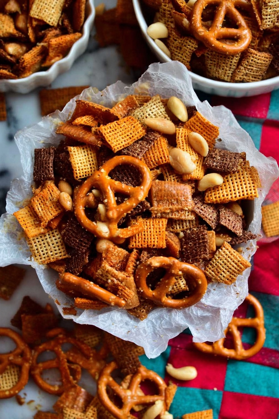 Christmas Savory Snack Mix, festive snack mix, holiday party snacks, savory holiday mix, crunchy holiday treats - A close-up of a mix of snacks piled in a bowl lined with white parchment paper, sitting on a white marbled surface; the mix shows layers of light orange square crackers with a smooth texture, dark brown woven cereal pieces with a rough texture, golden pretzels with a shiny surface and salt specks, and small pale yellow peanuts scattered throughout. The background has a colorful checkered cloth with red, turquoise, and beige squares, adding contrast to the snack pile. Some of the snack mix is spilled outside the bowl onto the marbled surface, with two white bowls partially visible containing more of the same snack mix. photo taken with an iphone --ar 2:3 --v 7