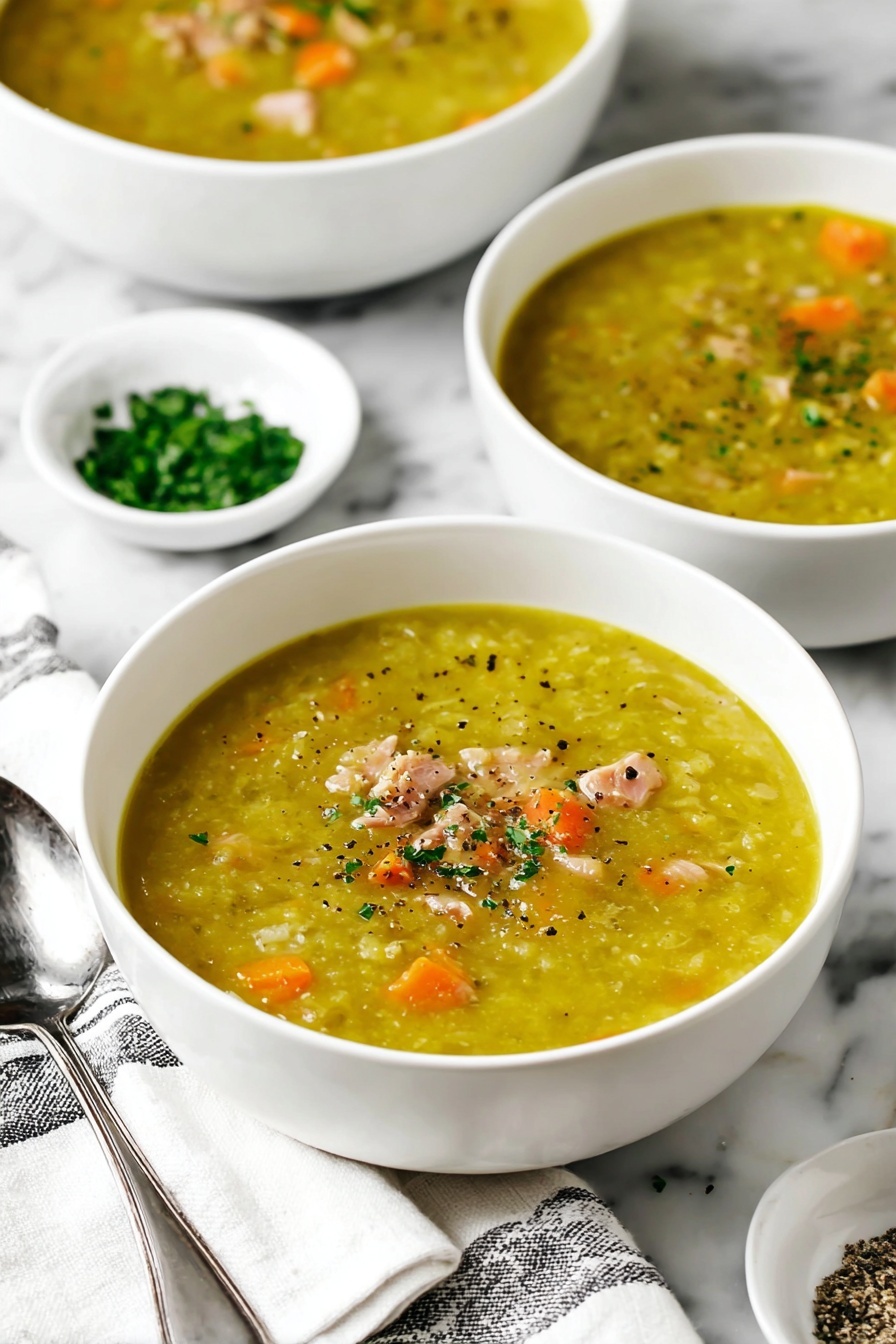 Hearty Split Pea Soup, hearty split pea soup, easy split pea soup recipe, comforting pea soup, healthy split pea soup - The image shows a white bowl filled with thick yellow-green soup that has small pieces of orange carrot and light pink chunks of meat inside. The soup is topped with small green herb bits and black pepper. Another bowl of the same soup is behind it, slightly out of focus. To the right side, there are two small white bowls, one filled with chopped green herbs and the other with coarse salt and pepper. A silver spoon rests beside the front bowl on a white cloth with black stripes, all placed on a white marbled surface. Photo taken with an iphone --ar 2:3 --v 7