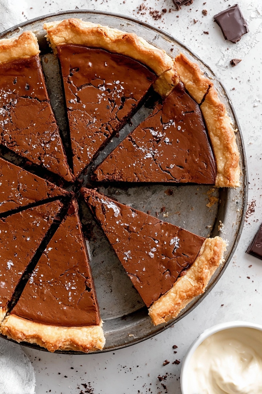 Fudgy Chocolate Brownie Pie, chocolate brownie pie, decadent brownie tart, chocolate dessert, homemade brownie pie - The image shows a round pie cut into six slices. The pie has a thick, shiny, dark brown top layer with a cracked texture and a golden, flaky crust around the edges. The pie rests on a metal tray with a dark, worn finish. The background is a white marbled surface with scattered chocolate bits. At the bottom right corner, there's a small white bowl filled with smooth, light cream. photo taken with an iphone --ar 2:3 --v 7