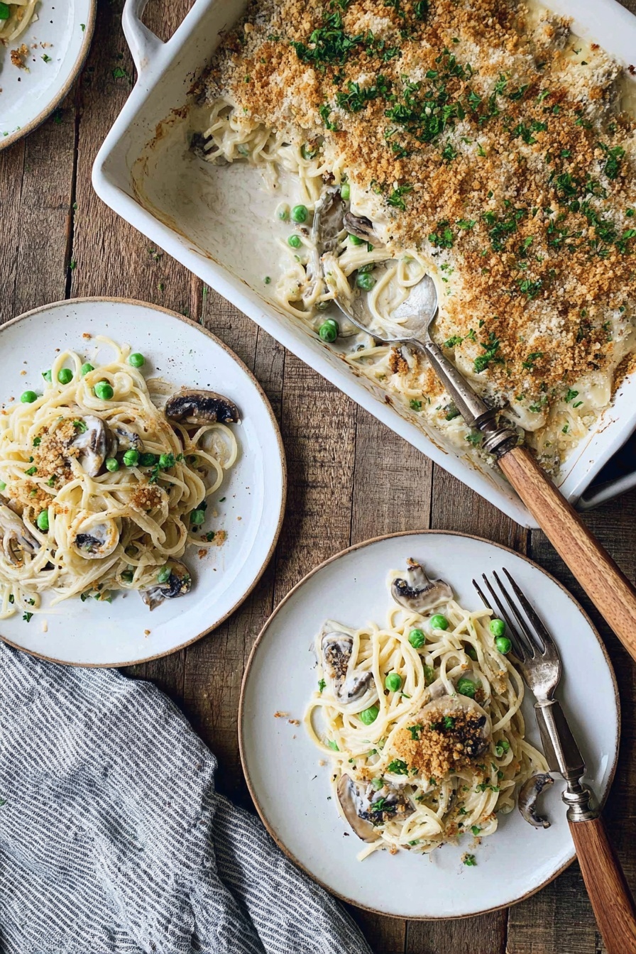 Creamy Turkey Tetrazzini Bake, Turkey Tetrazzini casserole, easy Turkey Tetrazzini, comforting pasta bake, cheesy turkey casserole - The image shows a white rectangular baking dish filled with a creamy spaghetti casserole topped with a golden brown breadcrumb crust and sprinkled with chopped green herbs. Inside the dish, there are visible green peas and slices of dark mushrooms mixed with the creamy pasta. Two servings of the casserole have been plated separately on white round plates, each layered with creamy white sauce spaghetti, green peas, and mushrooms, and garnished with crumbs and herbs. A silver fork with a wooden handle rests on the main plate. The setting is on a rustic wooden table with a gray and white striped cloth nearby. Photo taken with an iphone --ar 2:3 --v 7
