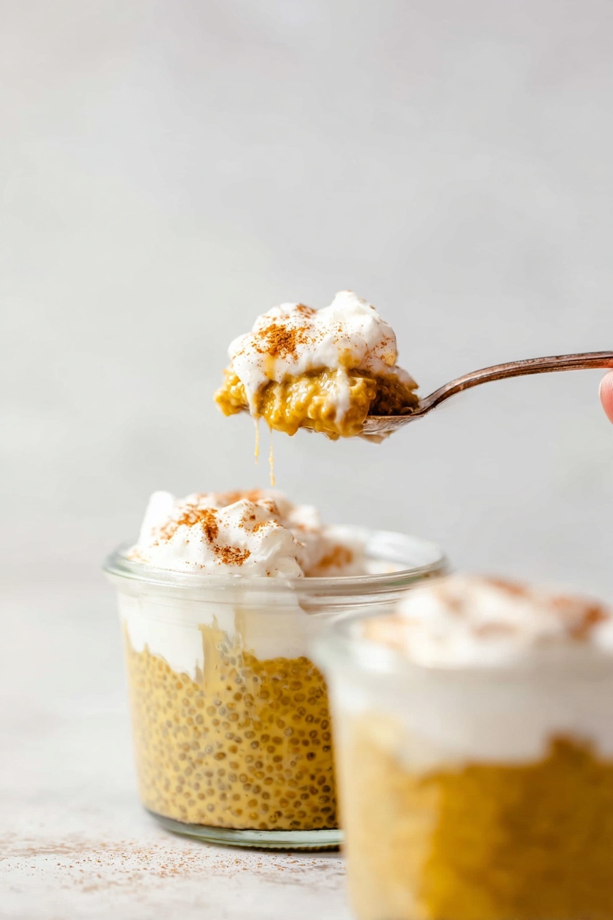 Healthy Pumpkin Chia Seed Pudding, Pumpkin Chia Seed Pudding, Nourishing Pumpkin Pudding, Easy Pumpkin Dessert, Wholesome Pumpkin Snack - The image shows a spoon holding a small scoop of a layered dessert with two clear glass jars filled with the same dessert in the background. The bottom layer in the jars is a yellowish-brown pudding with visible chia seeds, giving it a slightly bumpy texture. On top of the pudding is a thick, white cream layer lightly dusted with a brown spice, likely cinnamon. One jar has a woman’s hand partly visible holding a spoon covered with the white cream layer and some pudding drips on the rim. The background and surface are smooth with a white marbled texture. photo taken with an iphone --ar 2:3 --v 7