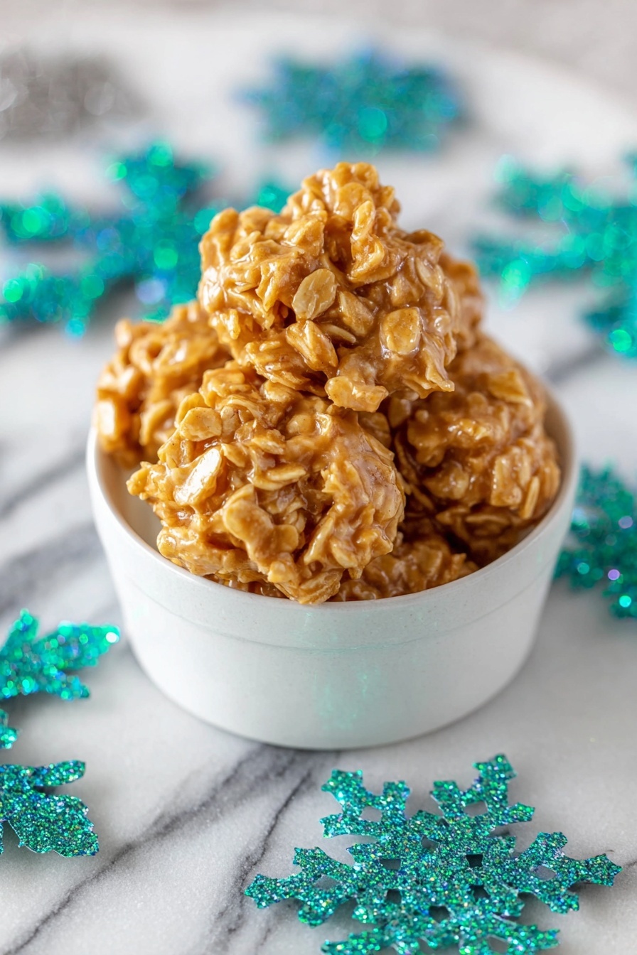 Peanut Butter Cornflake Candy, no-bake candy recipes, easy homemade treats, sweet salty crunchy snacks, quick peanut butter snacks - A white bowl decorated with green pine tree patterns and white dots holds five round clusters of a golden-orange snack with a sticky, shiny texture and small visible flakes in each cluster. The bowl is placed on a white marbled surface scattered with large, glittery turquoise and teal snowflake shapes. The clusters look thick and uneven with rough edges. Photo taken with an iphone --ar 2:3 --v 7