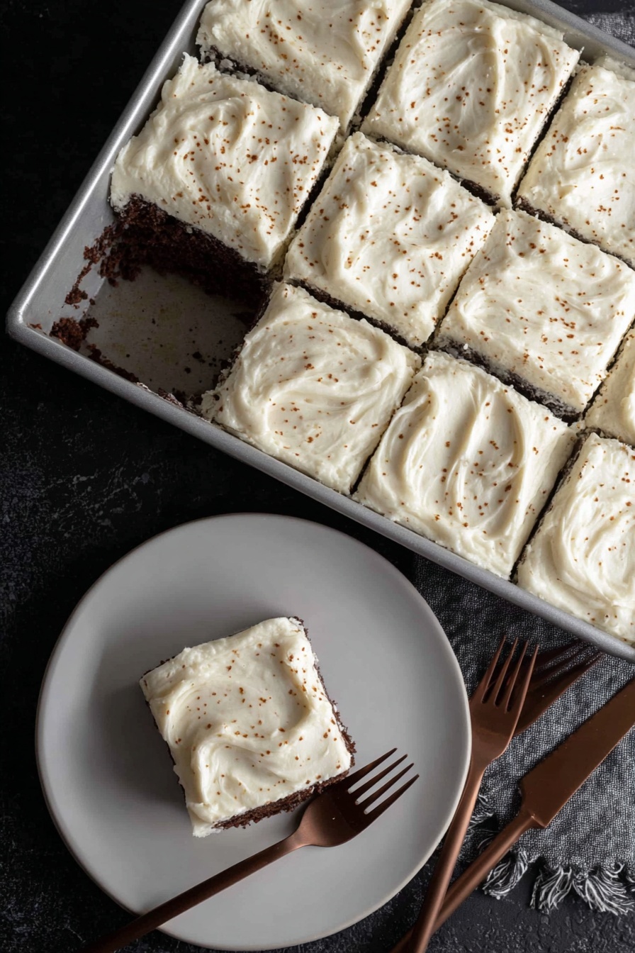 Dark Chocolate Espresso Cake without recipe, decadent chocolate cake, espresso dessert, brown butter frosting recipe, rich chocolate cake with espresso - A rectangular metal pan holds a cake cut into nine square pieces, with one piece missing near the center showing a dark, moist chocolate layer under a thick, creamy white frosting. Each frosting layer is spread thick and smooth with slight swirling patterns and small brown specks sprinkled over the top. On a white plate below, one square piece of the cake sits with the same thick white frosting on top and dark chocolate cake layer visible on the sides. Two brown forks lie near the plate on a black textured surface. photo taken with an iphone --ar 2:3 --v 7