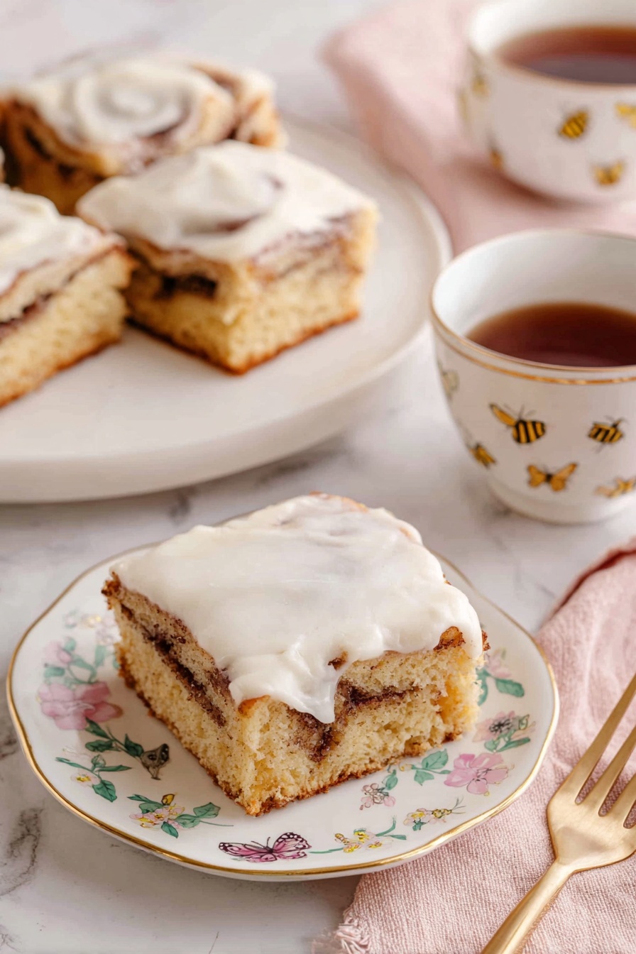 Cinnamon Roll Cake, easy cinnamon roll cake, moist cinnamon cake, cinnamon swirl cake, breakfast cake recipes - The image shows three square pieces of cinnamon roll cake with a light brown base and a visible swirl of darker cinnamon filling inside. Each piece is topped with a thick, creamy white icing that spreads unevenly on top. The pieces sit on white plates with delicate gold edges and small floral designs. A white teacup with a gold line on the rim and small floral pattern holds dark brown tea, positioned beside one of the plates. A gold fork rests on a soft pink napkin near the front plate. The background is a white marbled surface, and a tray with more pieces is visible in the back. Photo taken with an iphone --ar 2:3 --v 7
