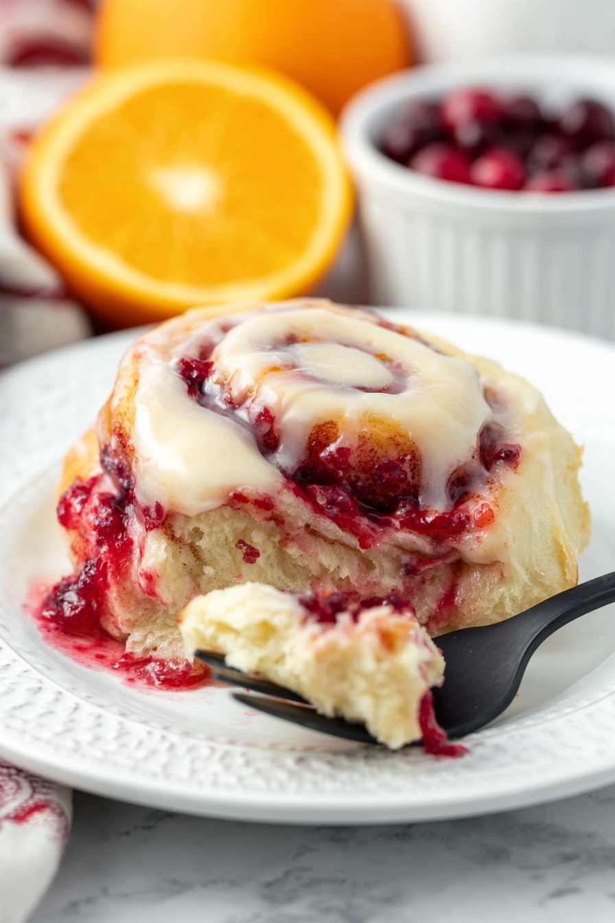 Cranberry Orange Sweet Rolls, citrus cranberry breakfast rolls, fluffy cranberry orange pastry, easy sweet rolls with cranberries, holiday orange cranberry baked goods - The dish shows a soft, swirled roll with three main layers: a creamy white icing layer on top that looks smooth and rich, a middle layer with a light beige dough, and a bright red layer of berry filling that appears juicy and slightly thick, seeping out from the roll. The roll is on a white plate with gentle embossed patterns, against a white marbled background. In the front, a black fork holds a small piece of the roll with some berry filling and dough, and in the back, blurred slices of orange and a white bowl filled with deep red cherries add color contrast. Photo taken with an iphone --ar 2:3 --v 7