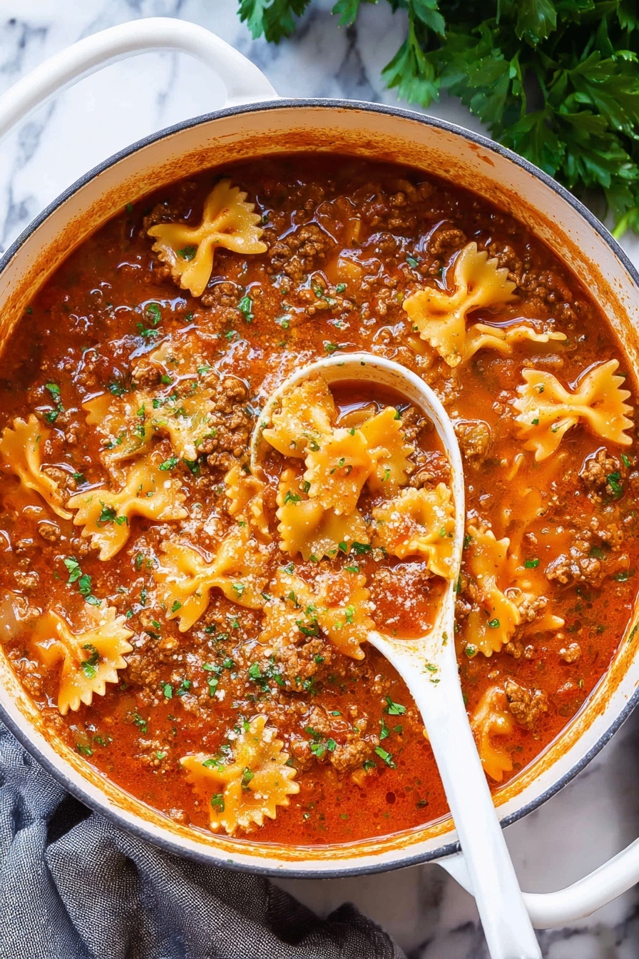 Lasagna Soup, easy lasagna soup, comforting lasagna soup, Italian lasagna soup, quick lasagna soup - A large white pot filled with a rich, thick soup showing three main layers: a red tomato broth with a slightly oily surface, small chunks of brown cooked meat spread throughout, and pale orange bow-tie shaped pasta floating on top, sprinkled with small pieces of chopped green herbs. A white spoon is partly dipped in the soup revealing the sauce's thickness and layered textures. The pot is placed on a white marbled surface with some green herbs in the background and a gray cloth to the side, photo taken with an iphone --ar 2:3 --v 7