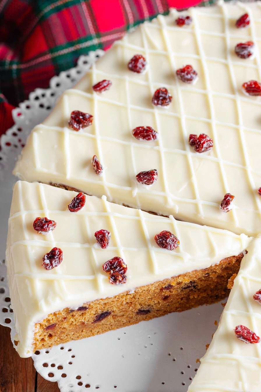 Cranberry White Chocolate Bliss Bars, cranberry white chocolate bars, holiday cranberry bars, easy cranberry dessert, white chocolate cranberry treats - A single slice of cake is shown on a white decorative plate with small cut-out patterns. The cake has two clear layers: a dense golden-brown base with visible small dark red dried fruit pieces inside, and a thick smooth white icing layer on top, decorated with a white grid pattern and scattered dark red dried fruit pieces. The plate rests on a wooden surface with a blurred part of the whole cake and a red and green fabric in the background. Photo taken with an iphone --ar 2:3 --v 7
