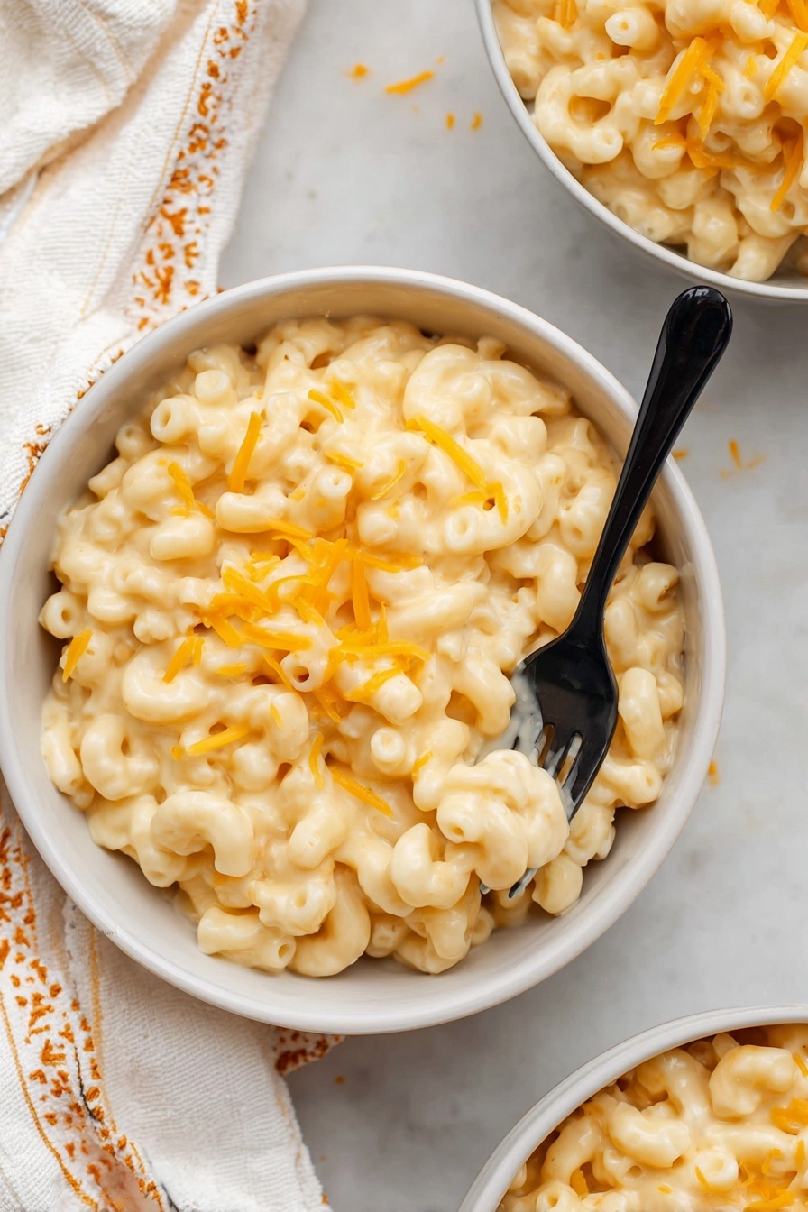 Stovetop Mac and Cheese, creamy mac and cheese, homemade mac and cheese, quick stovetop mac and cheese, cheesy pasta recipe - A close-up view of creamy macaroni and cheese inside a white pot with a black rim. The macaroni is elbow-shaped, covered in smooth, pale yellow cheese sauce, with some small melted orange cheese bits sprinkled on top. A wooden spoon with a visible grain is scooping a portion of the cheesy macaroni, lifting it slightly above the pot. The pot sits on a light fabric with a yellow and white geometric pattern, all on a white marbled surface. Photo taken with an iphone --ar 2:3 --v 7