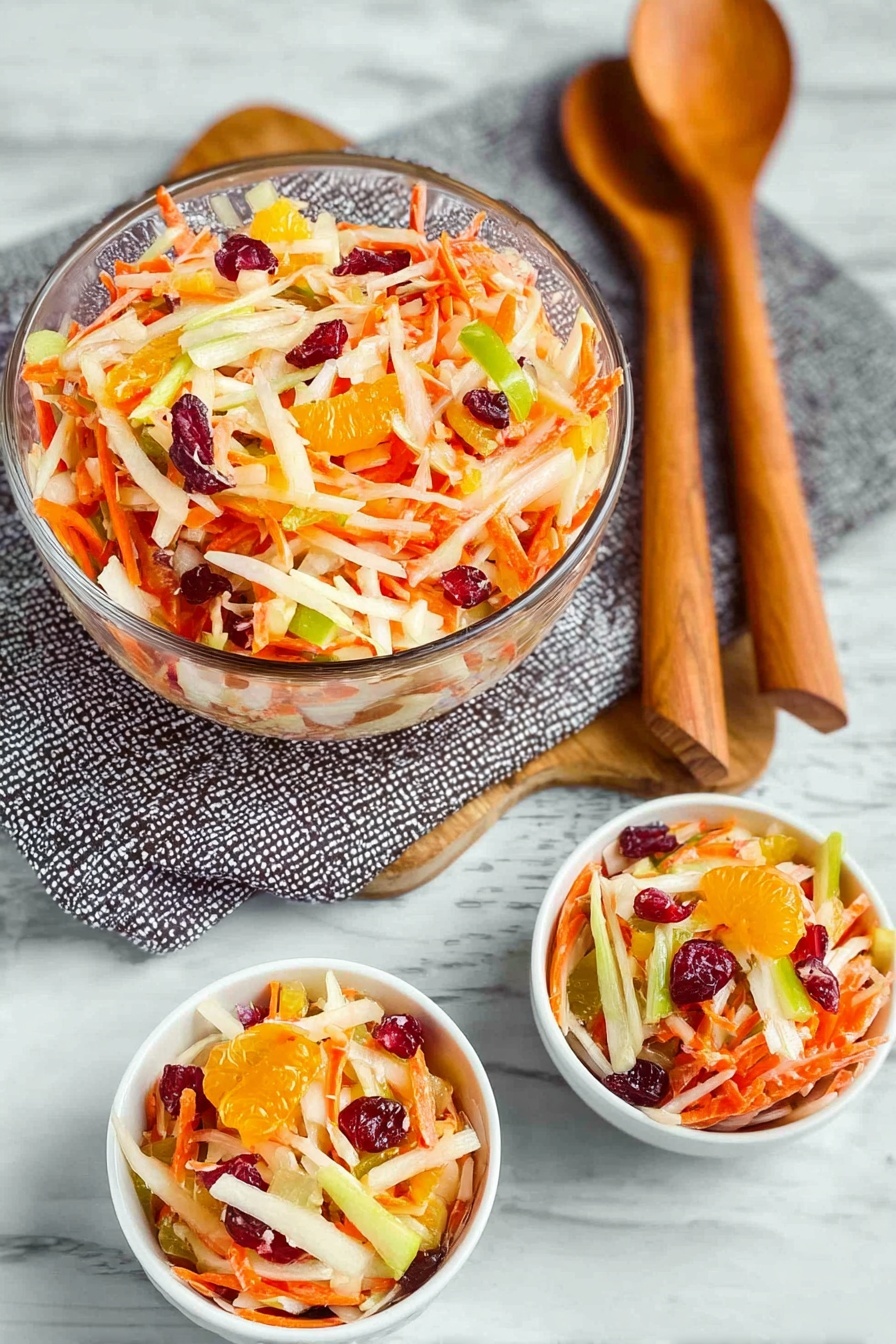 Carrot Apple Salad with Cranberries and Mandarins, healthy fruit salad idea, easy autumn salad, fresh fruit salad recipe, colorful citrus carrot salad - A clear glass bowl filled with a colorful salad sits on top of a wooden salad spoon and fork resting on a gray patterned cloth, all placed on a white marbled surface. The salad shows layers of thin orange carrot strips, creamy white slivers of apple, green apple slices, bright orange mandarin pieces, and dark red dried cranberries or similar fruit mixed throughout. Two small white bowls in front also hold the salad, showing the same colorful mixture with vibrant orange, green, red, and creamy white pieces clearly visible. photo taken with an iphone --ar 2:3 --v 7